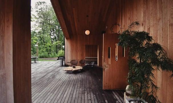 Wooden deck with modern outdoor seating under covered porch, surrounded by greenery