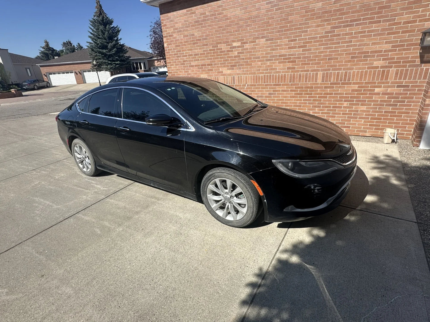 Black sedan parked on driveway beside brick house, showcasing vehicle protection for home and car investments