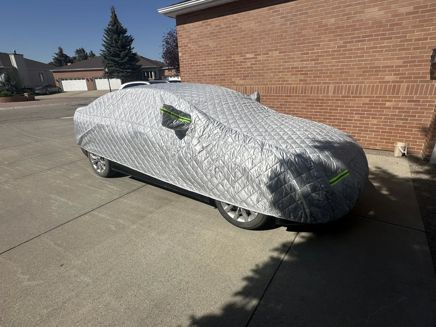 Silver quilted car cover with green stripes protecting vehicle from hail and sun in driveway